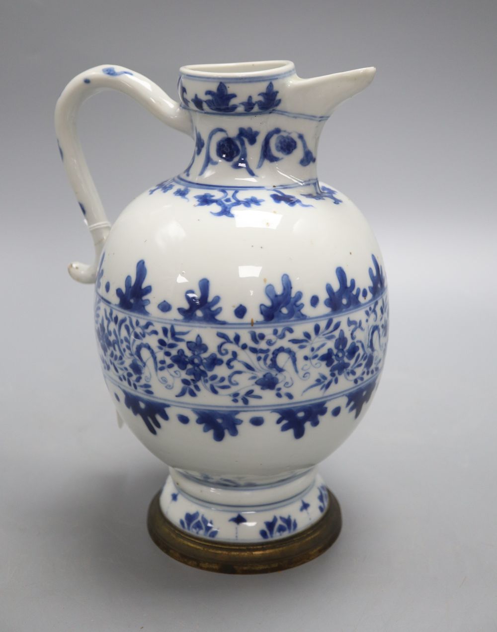 A Chinese blue and white ewer, Kangxi period, with a later brass mounted foot, 22cm high